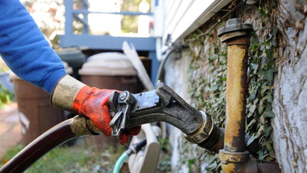Technician connecting fuel to an older oil tank fill pipe before priming the burner