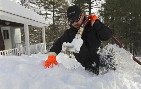 Driver clearing snow away from a buried oil tank fill pipe for a same-day delivery